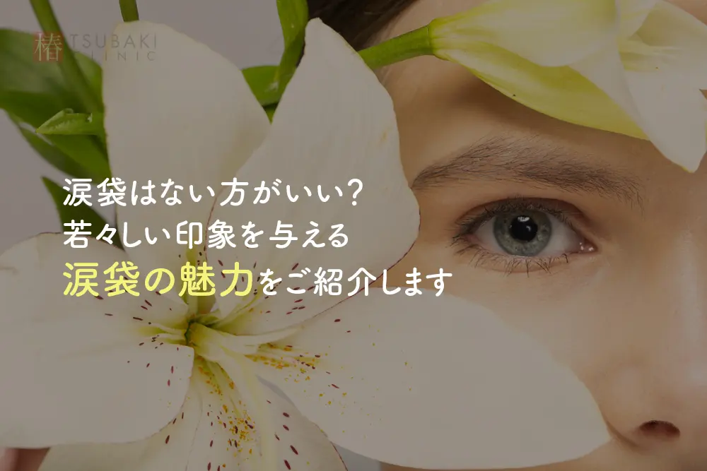 白いユリの花越しに、女性の片目と顔の一部が見えています。画像内には「涙袋はない方がいい？若々しい印象を与える涙袋の魅力をご紹介します」と書かれたタイトル画像です。