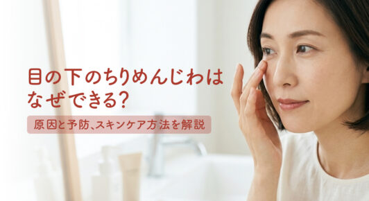目の下のちりめんじわを確認する女性の顔のアップ。「目の下のちりめんじわはなぜできる？原因と予防、スキンケア方法を解説」というタイトルの入った美容医療コラムのメインビジュアル。