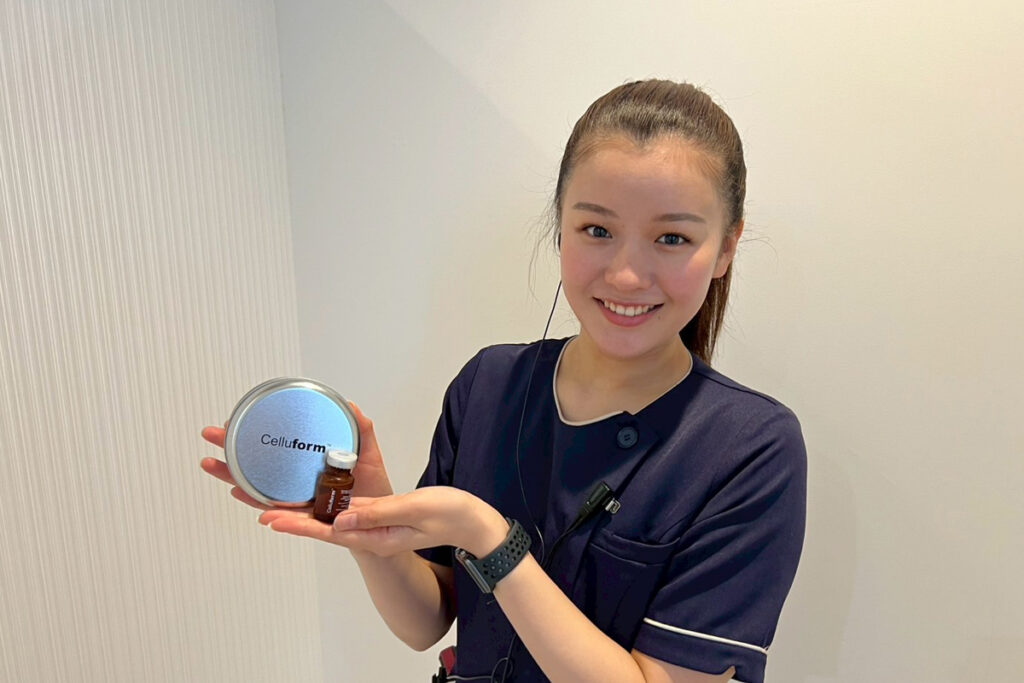 クリニックスタッフが笑顔で、脂肪溶解注射に使われる“Celluform”の丸い金属ケースと薬剤バイアルを両手で丁寧に掲げている様子。清潔感のある室内で、製品を紹介しているイメージ写真。
