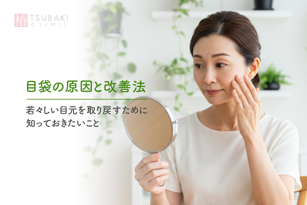 明るい部屋で、白い服の女性が手鏡を持ち、目の下（目袋）に指を当ててたるみを確認している。左側に「目袋の原因と改善法」「若々しい目元を取り戻すために知っておきたいこと」の文字があるコラムのタイトル画像